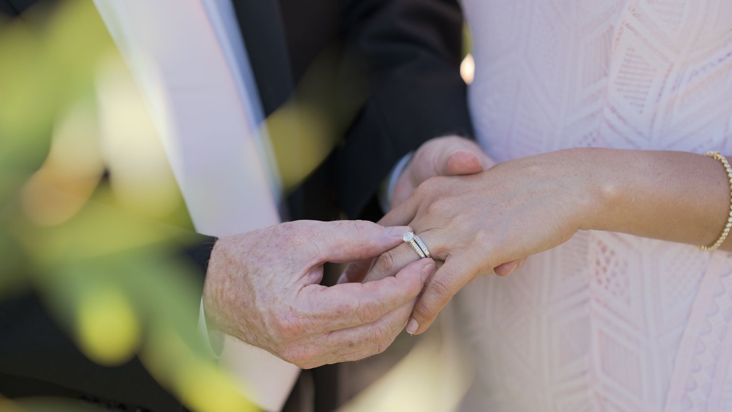 Close-up of hands exchanging rings during an outdoor wedding ceremony.