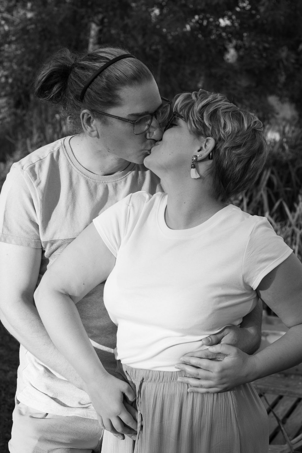 A romantic black and white portrait of a couple in white shirts sharing a tender moment outdoors.
