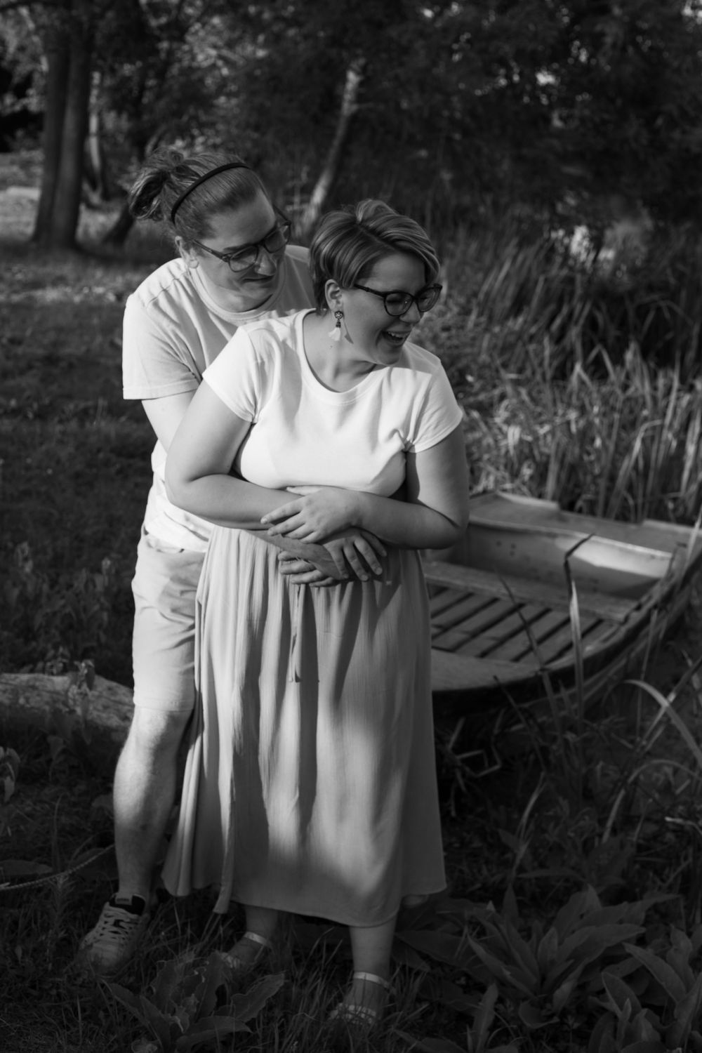 A couple embraces tenderly in a garden setting wearing casual white clothing.