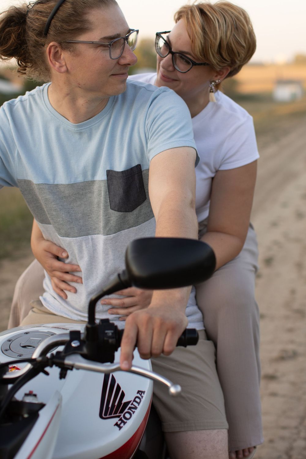 A couple poses together on a motorcycle, creating a romantic moment at sunset.