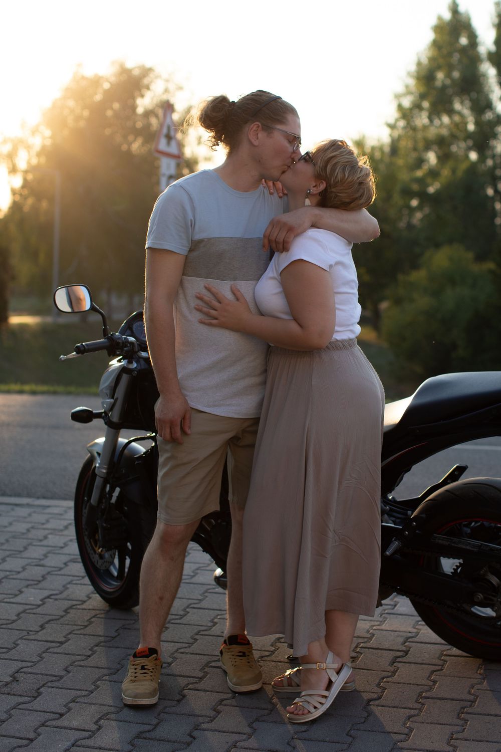 A romantic couple shares an intimate moment next to a motorcycle during golden hour sunset.