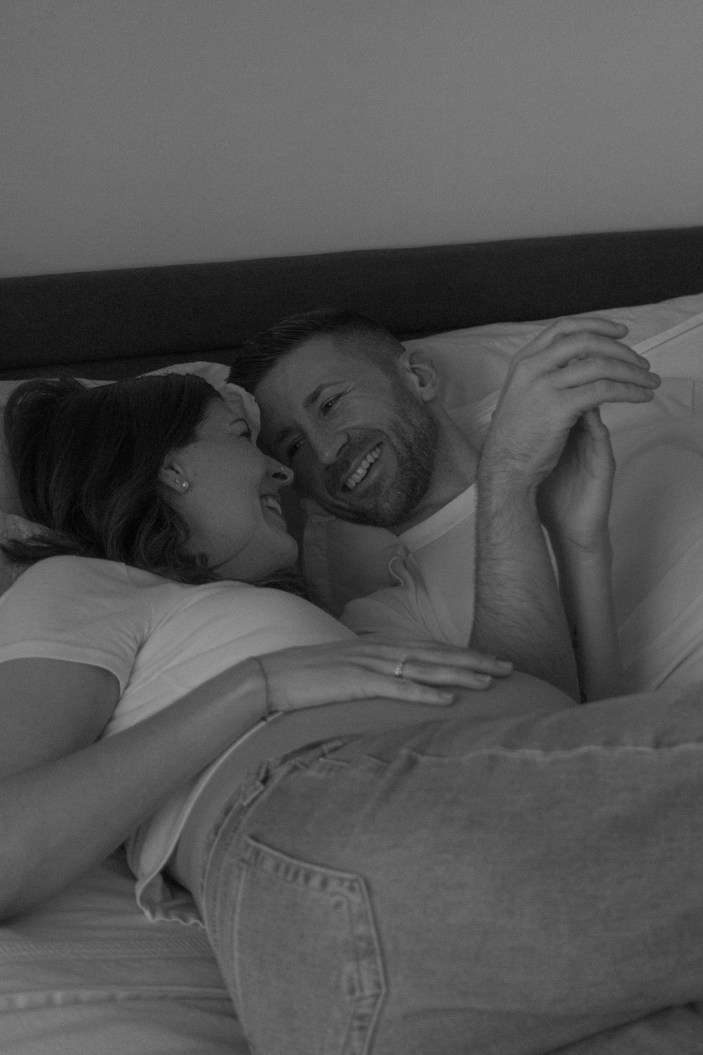 Black and white photo of a smiling couple lying together in bed, sharing a tender romantic moment.