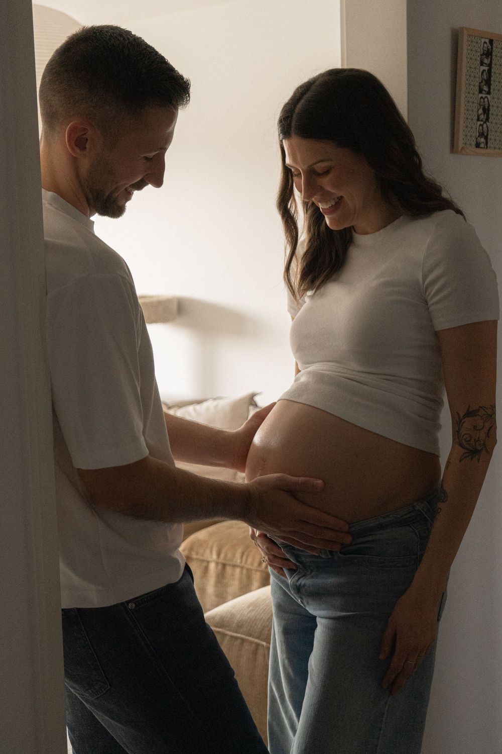 Happy couple sharing a tender moment as man gently touches pregnant woman's bare belly at home.