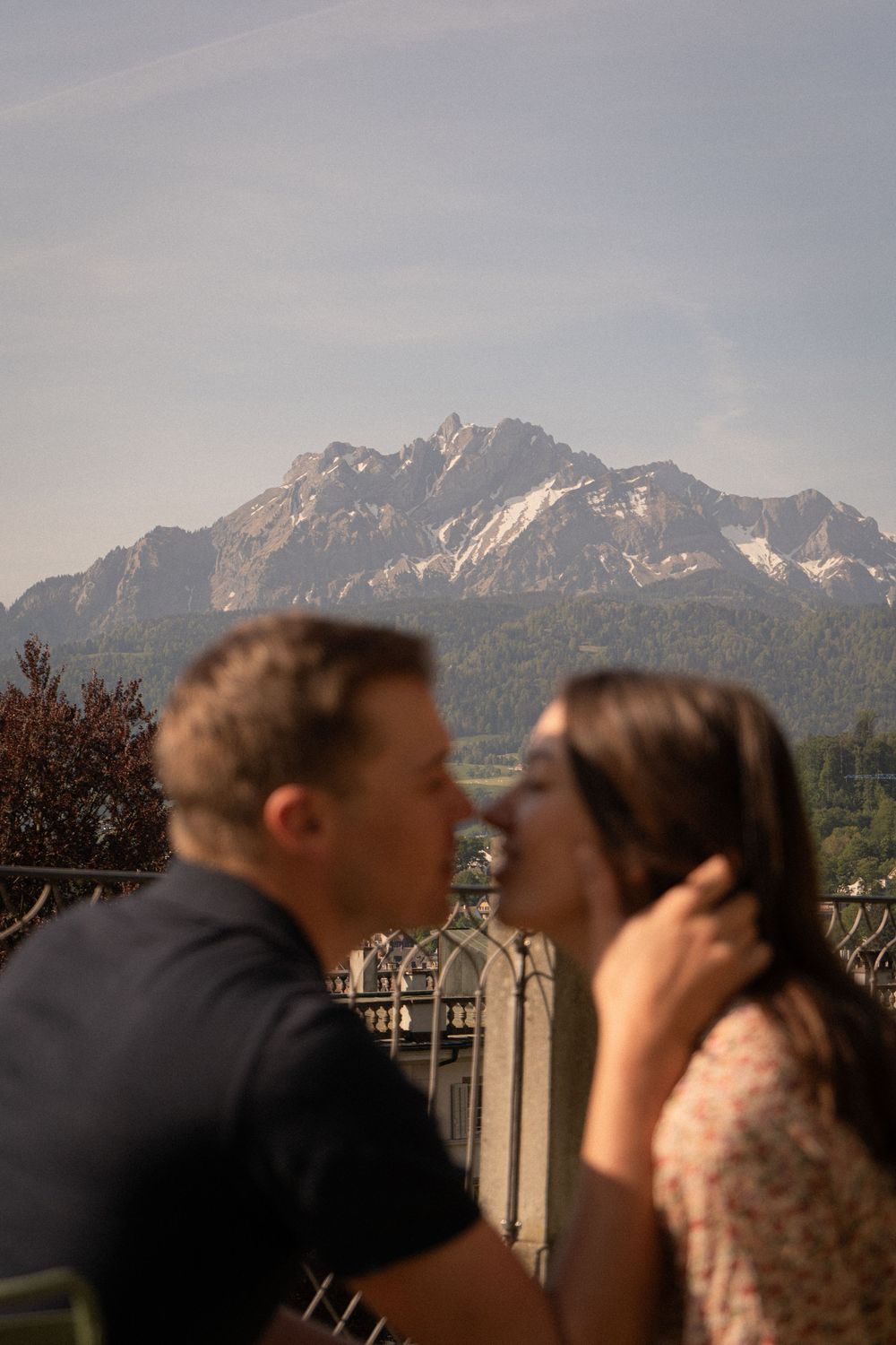 Couple sharing a romantic moment on a balcony with majestic mountain peaks in the background.