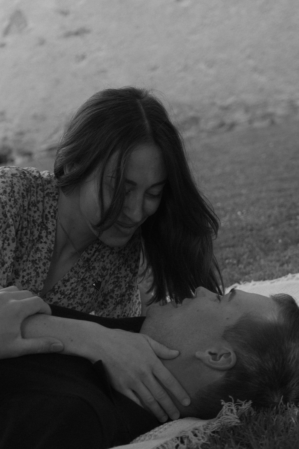 Black and white photo of a couple sharing a tender moment outdoors, woman leaning over man lying on grass.