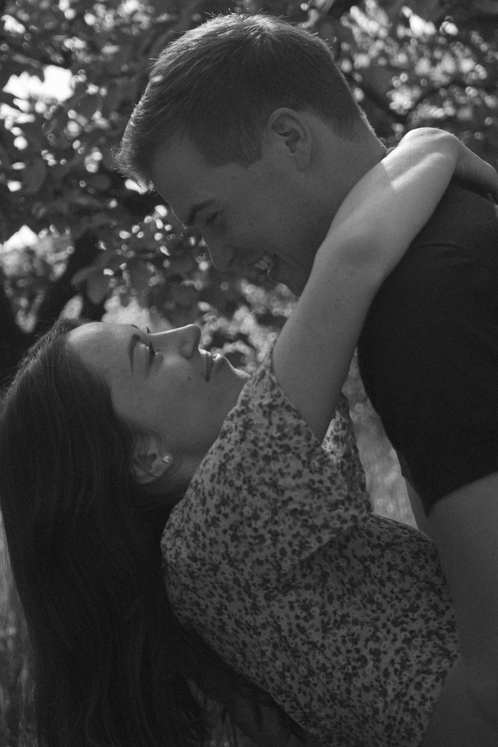 Black and white romantic couple embracing and gazing at each other under lush trees outdoors.
