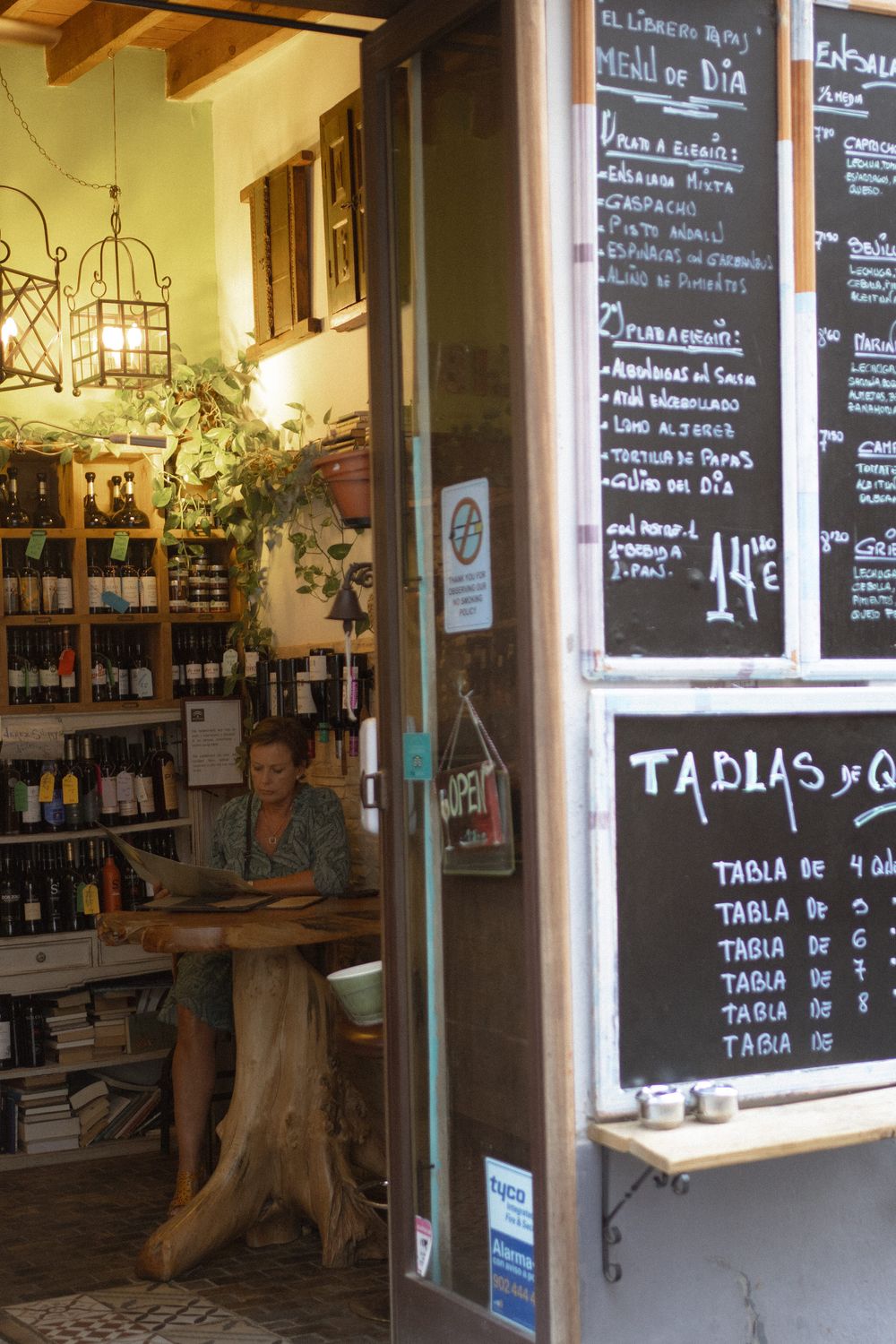 Small wine shop interior with wooden shelving and chalkboard menu displaying tapas prices and selections.