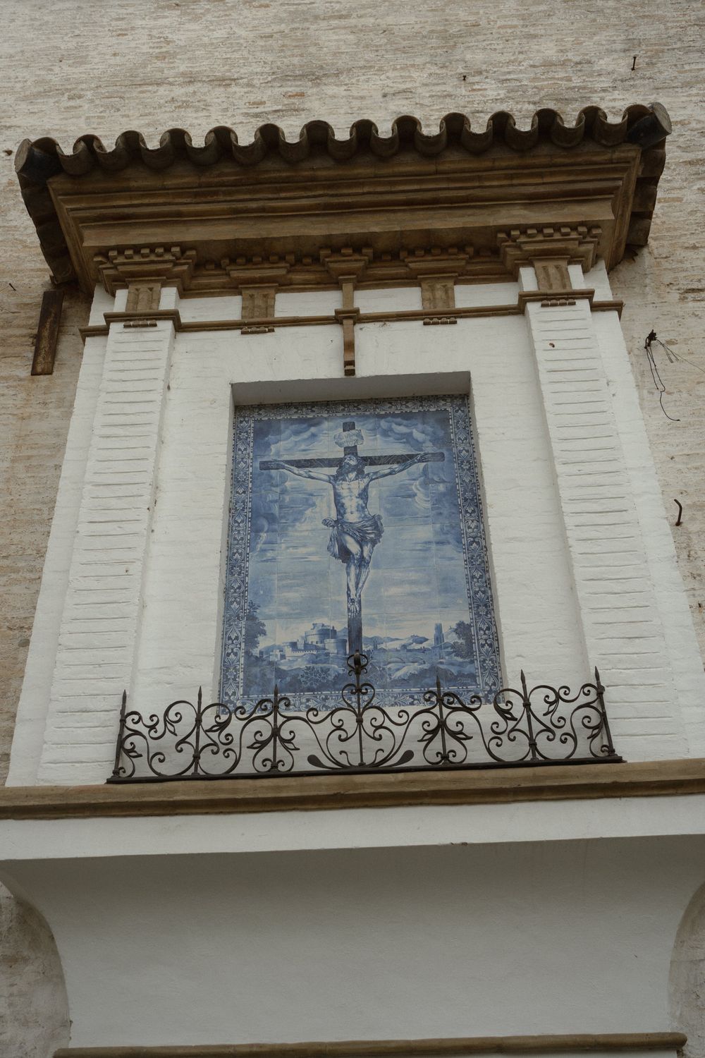 A blue and white ceramic tile depicting a crucifix mounted on a decorative white wall with ornate trim.
