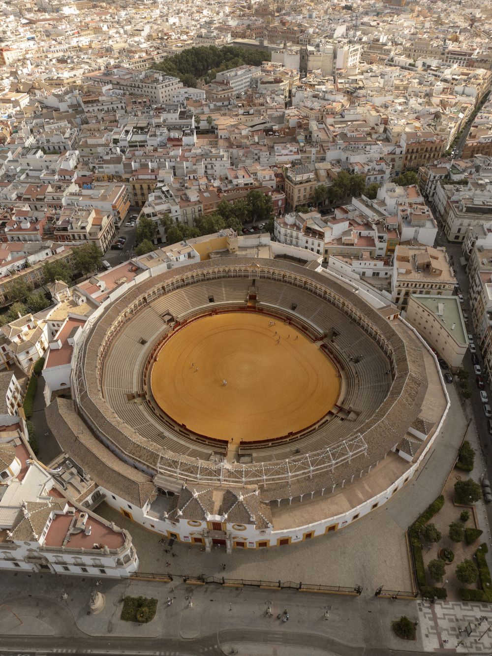 Aerial view of Plaza de Toros bullring in Seville showing its circular architecture and sandy arena from different angles.