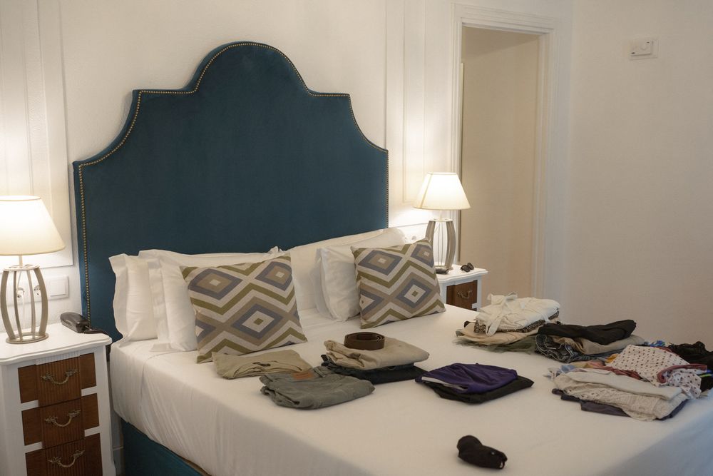 A modern bedroom interior with teal upholstered headboards, white bedding, and geometric patterned throw pillows.