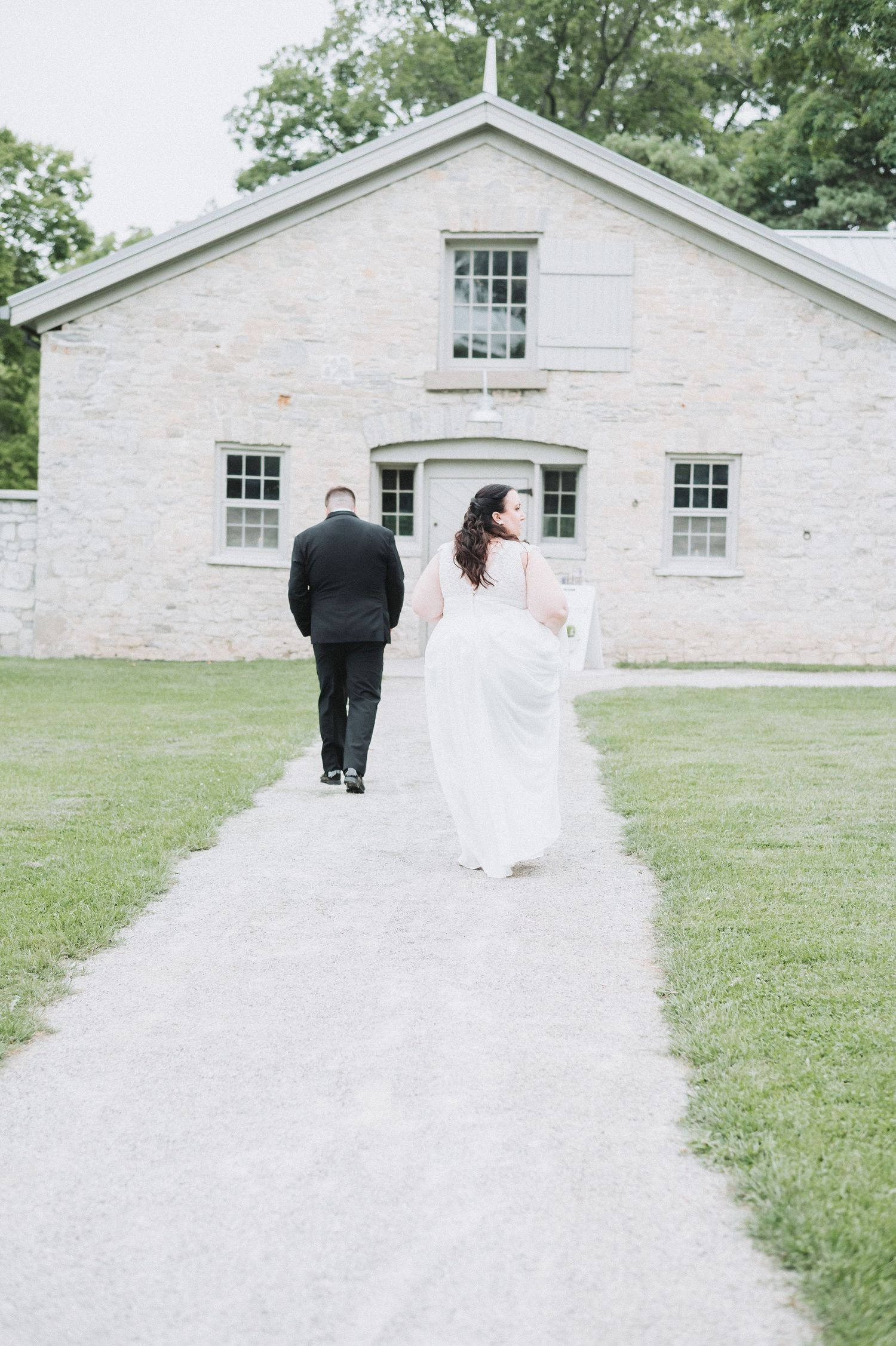A couple walks along a white stone path in front of a historic white building on a grassy lawn.