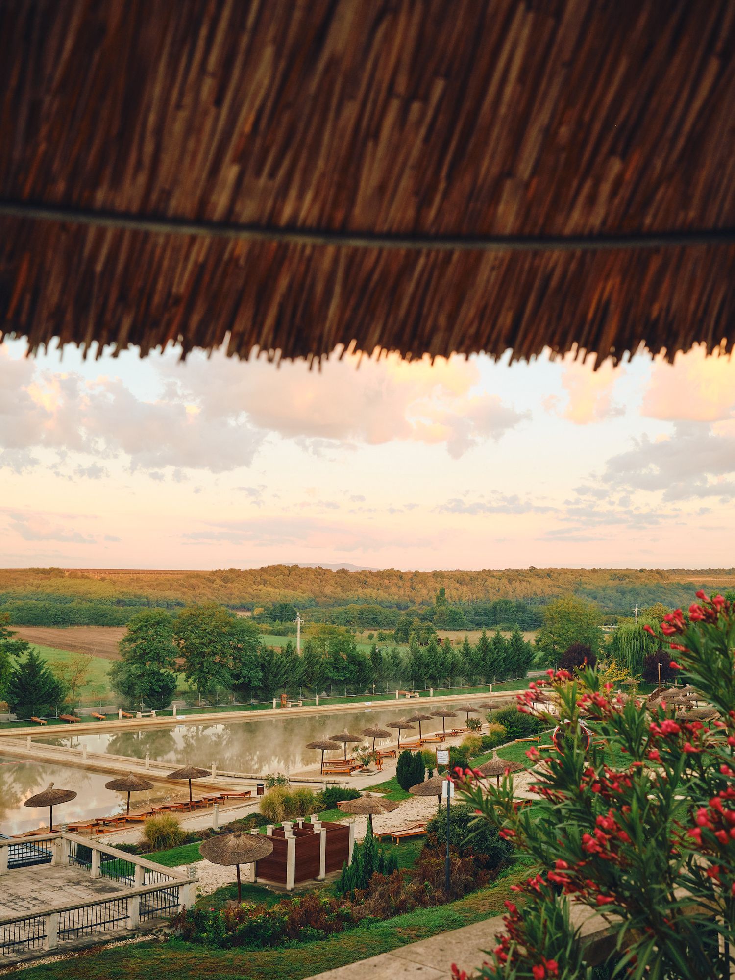Panoramic view of thatched roofs and red-tiled buildings overlooking a scenic rural landscape at sunset.