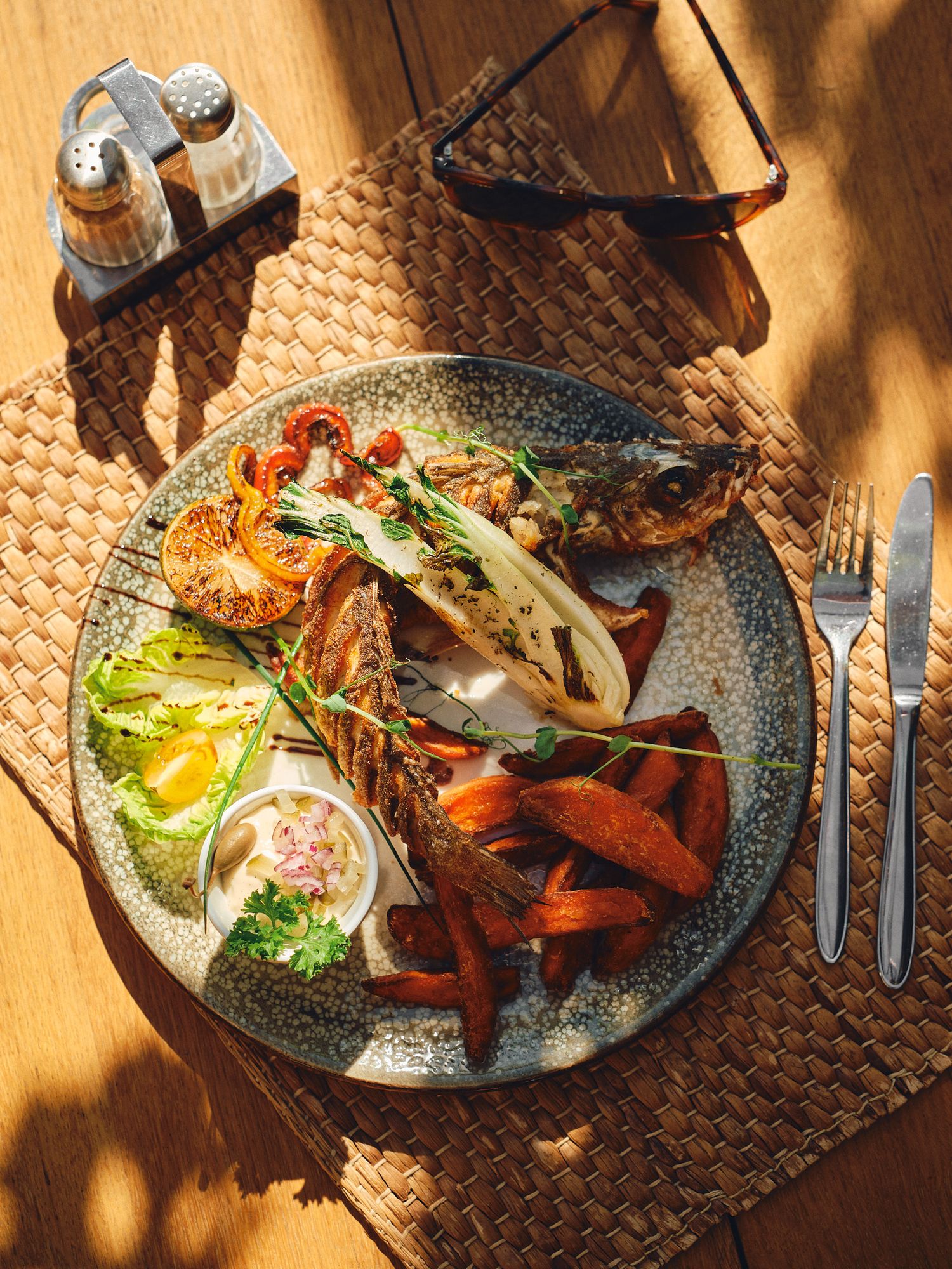 A gourmet seafood plate with grilled lobster, roasted vegetables, and white sauce served on a speckled ceramic dish.