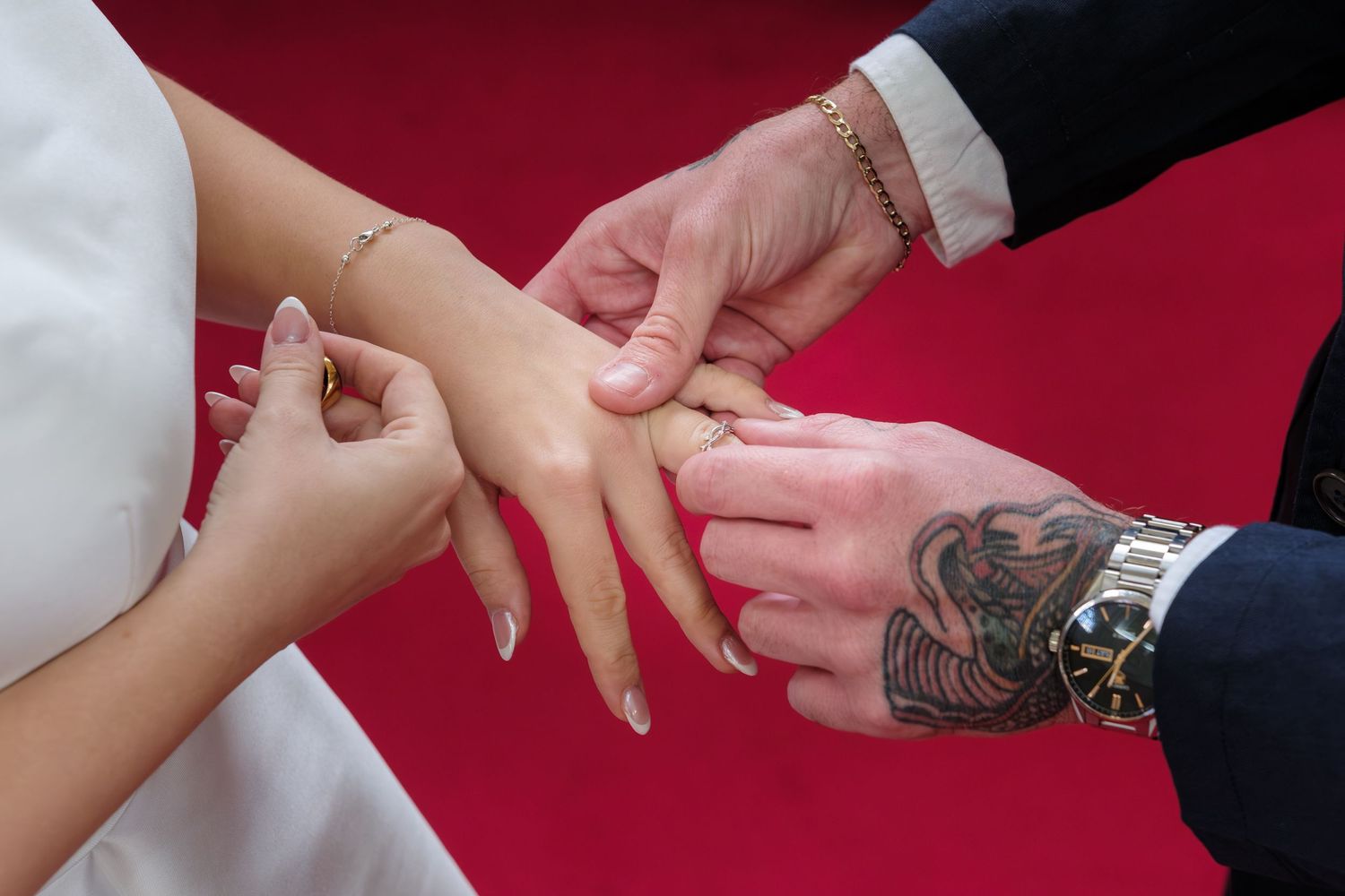 Close-up sequence of hands exchanging rings during a wedding ceremony against a red background.