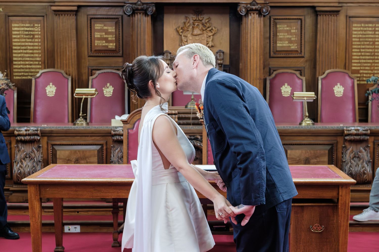 Two people sign official documents at a wooden courthouse desk during what appears to be a wedding ceremony.