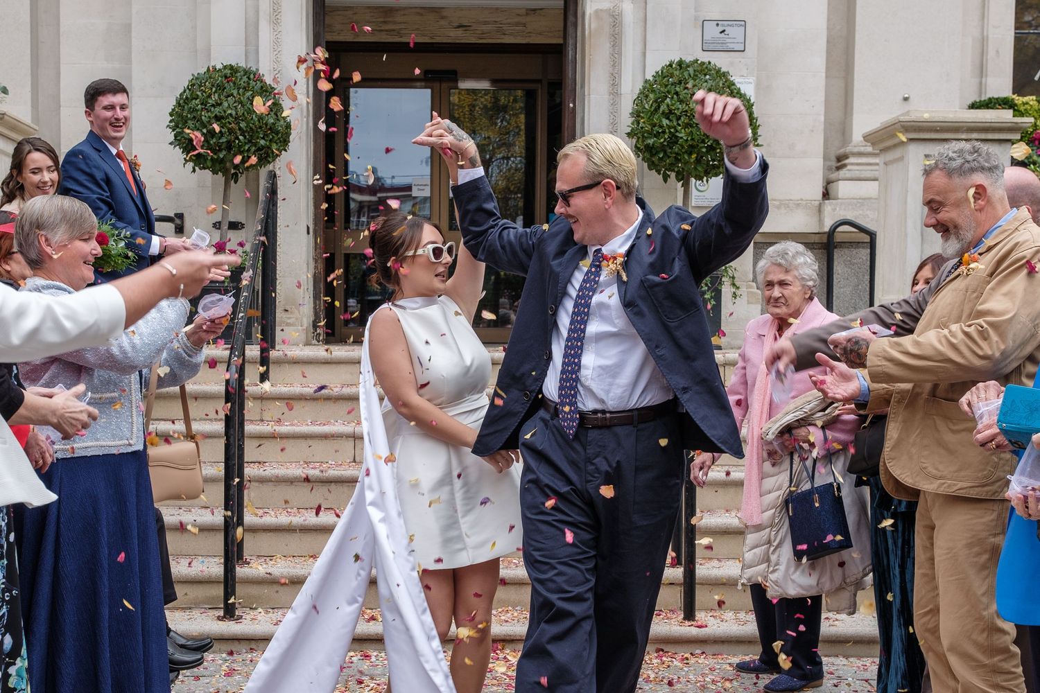 Wedding guests celebrate by blowing bubbles at a couple outside a church after their ceremony.