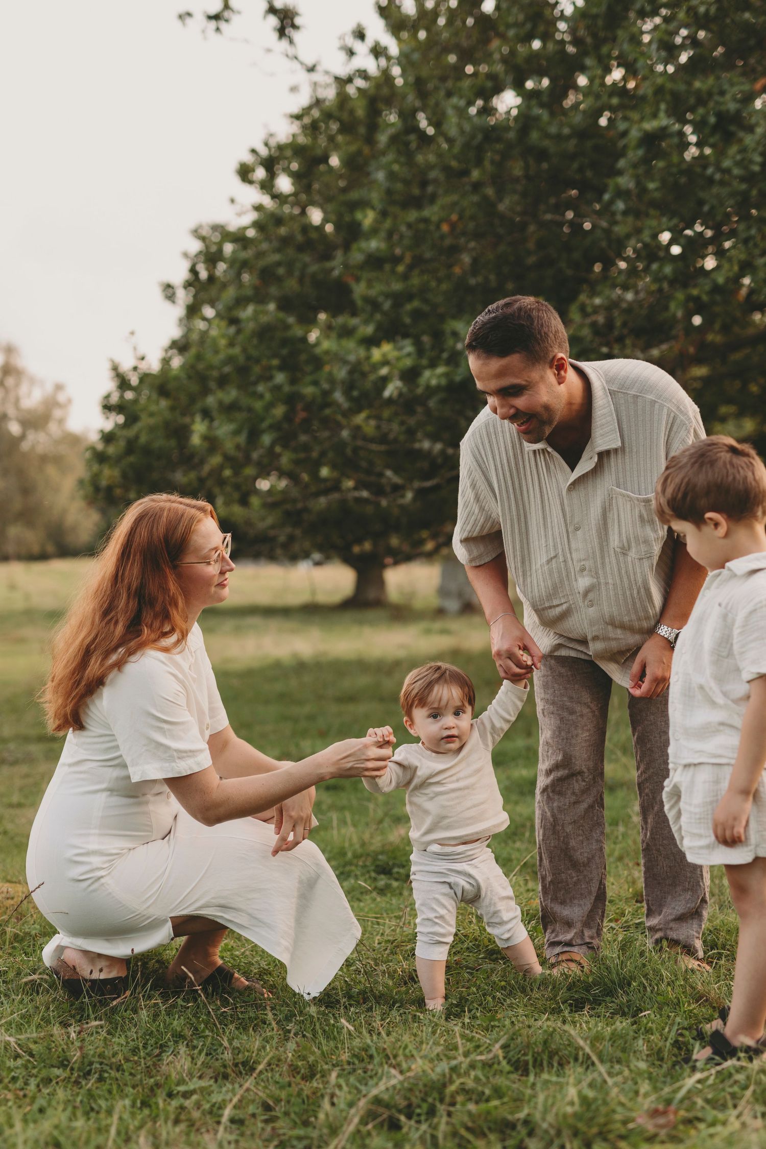 A playful family photoshoot in a grassy field wearing coordinated white and beige outfits.