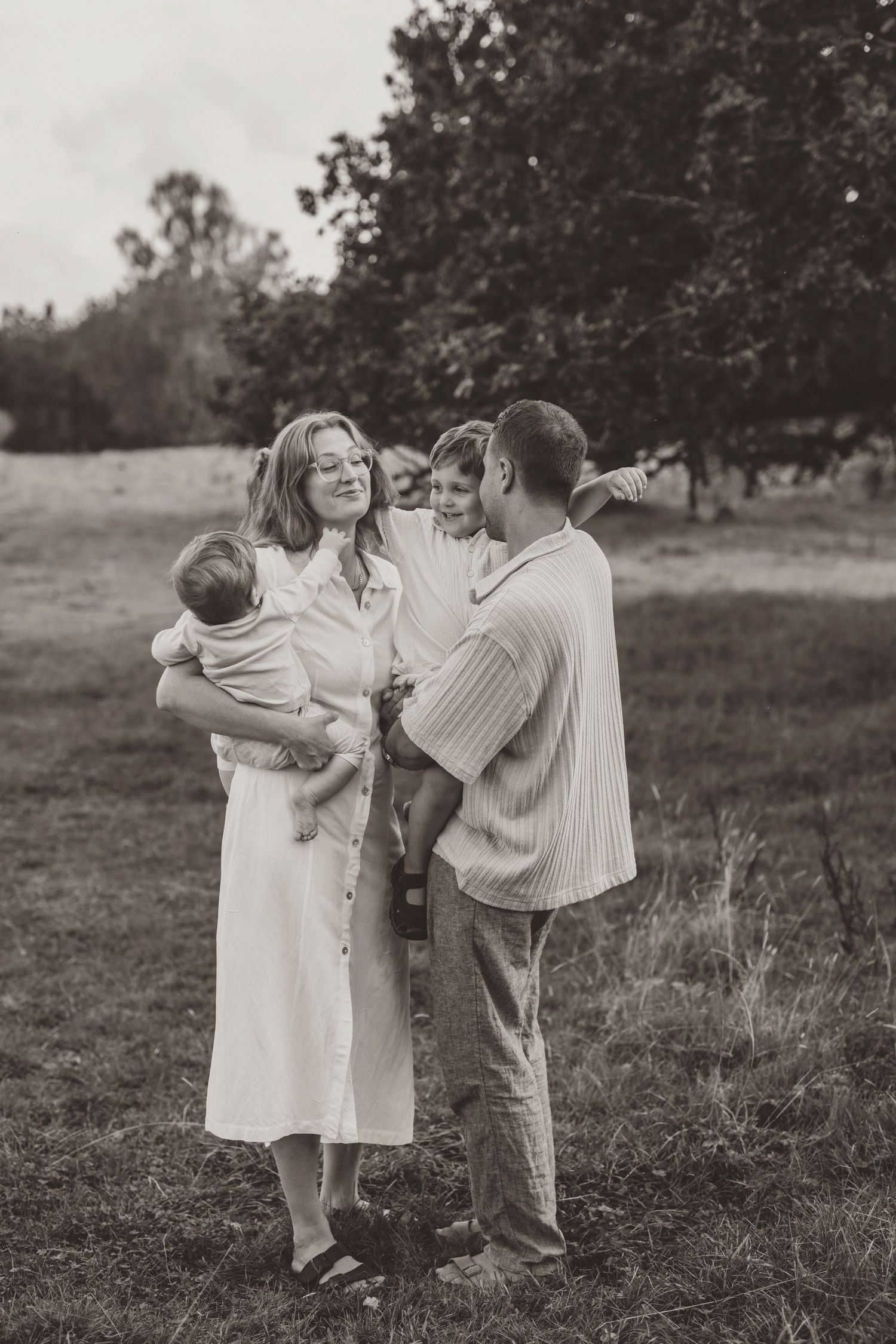 Black and white photo of a family embracing in a meadow, creating a heartwarming outdoor portrait.
