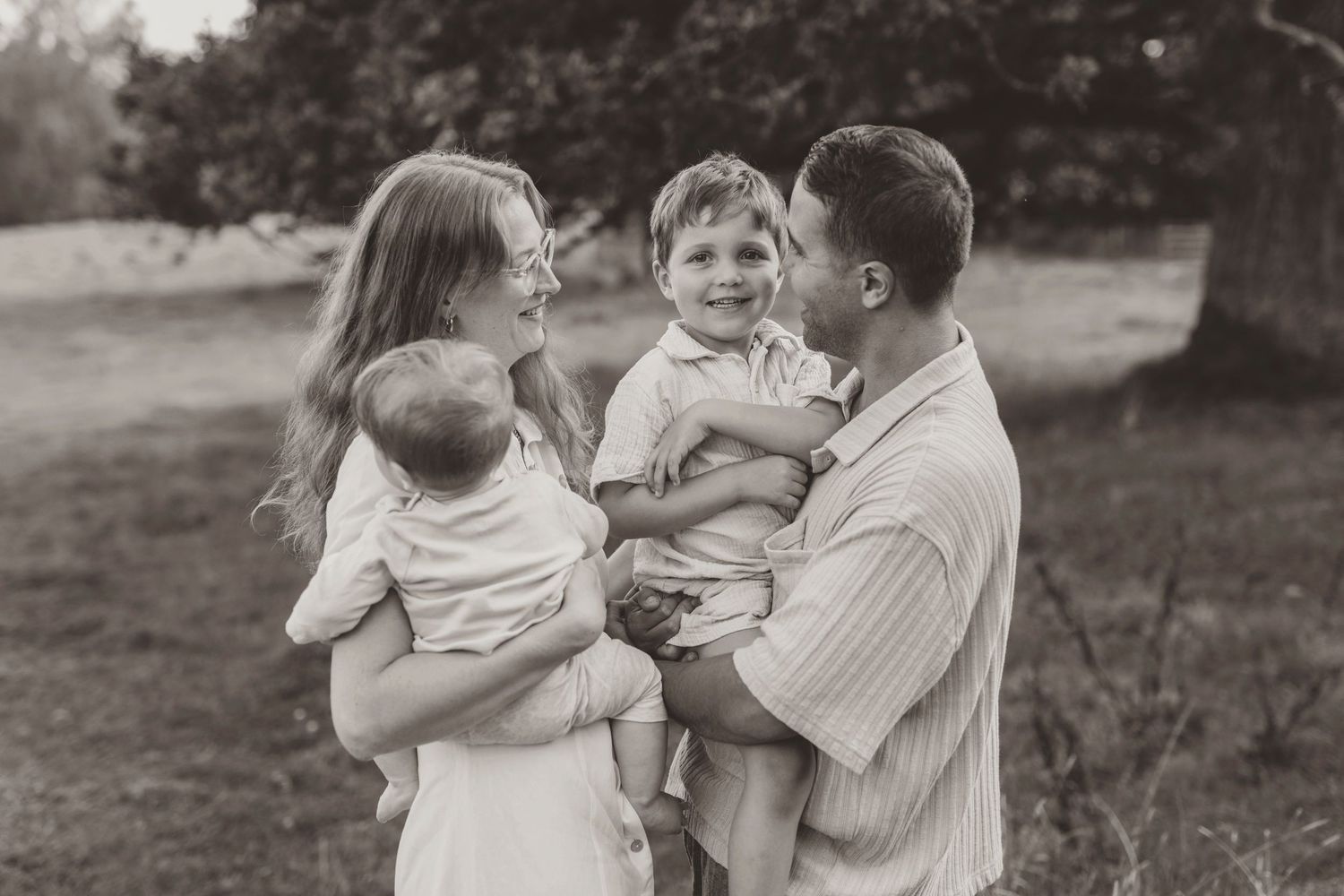 A series of black and white photos showing tender moments between young siblings and family members in an outdoor setting.