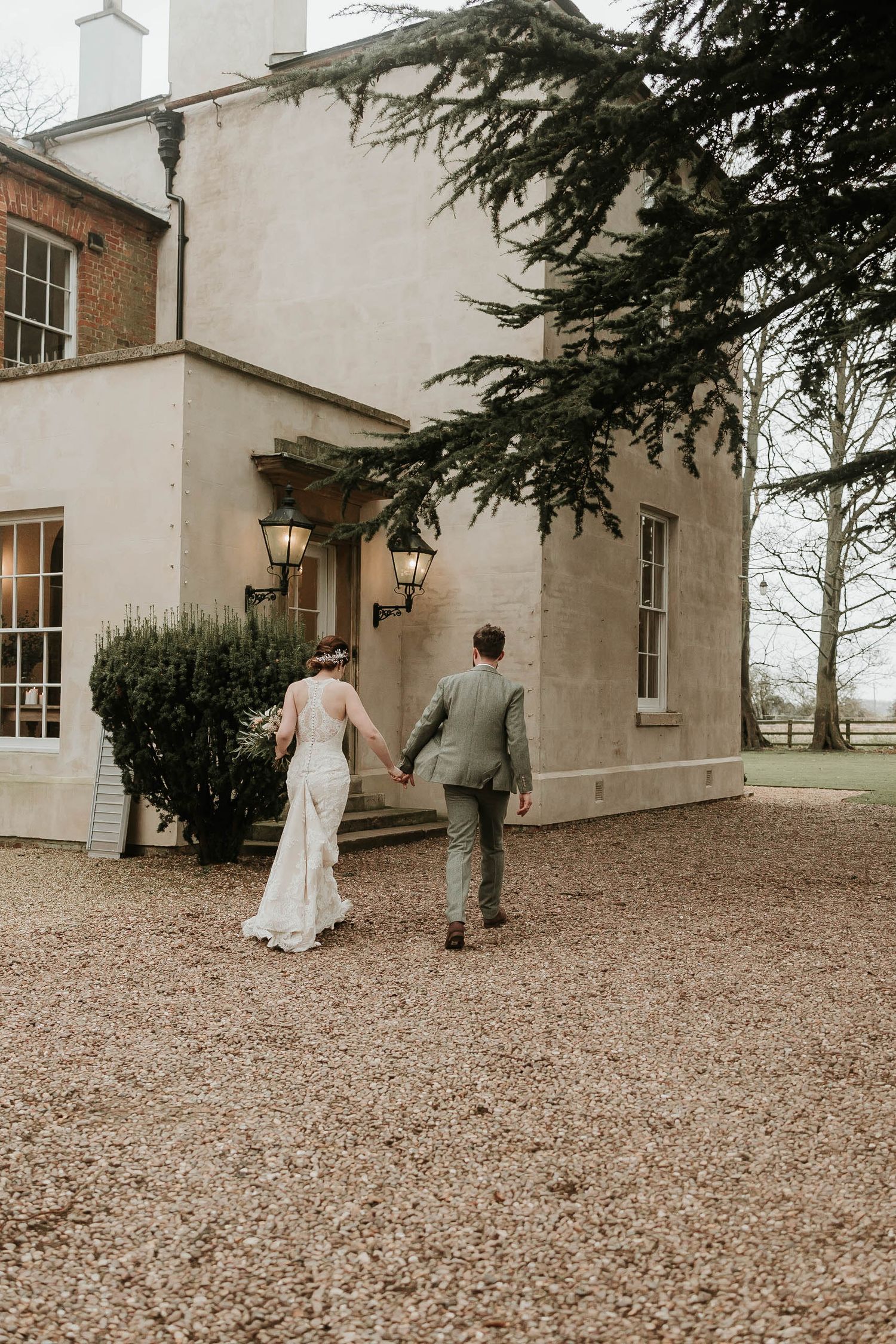 A couple walks along a gravel path towards a stately white building in a vintage-style photograph.
