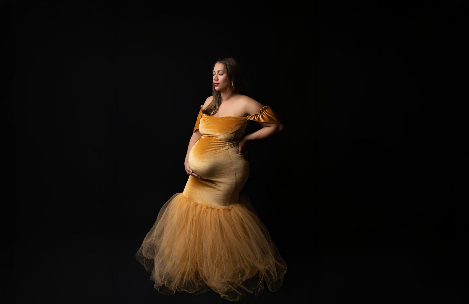 A woman's pregnant belly that is being poked by her young daugther's finger, no faces are visible.