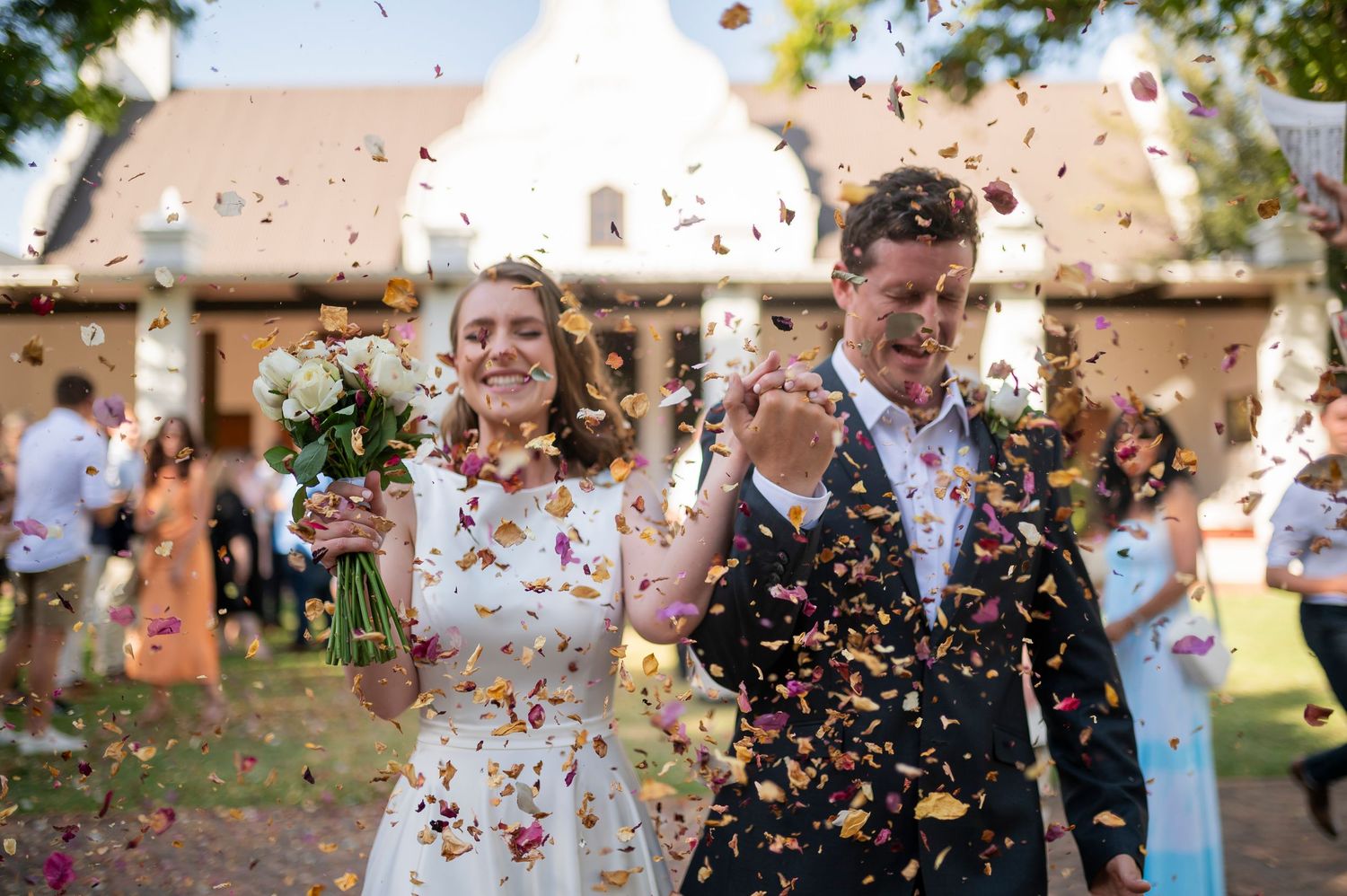 Wedding guests celebrate by throwing colorful confetti during outdoor reception festivities.
