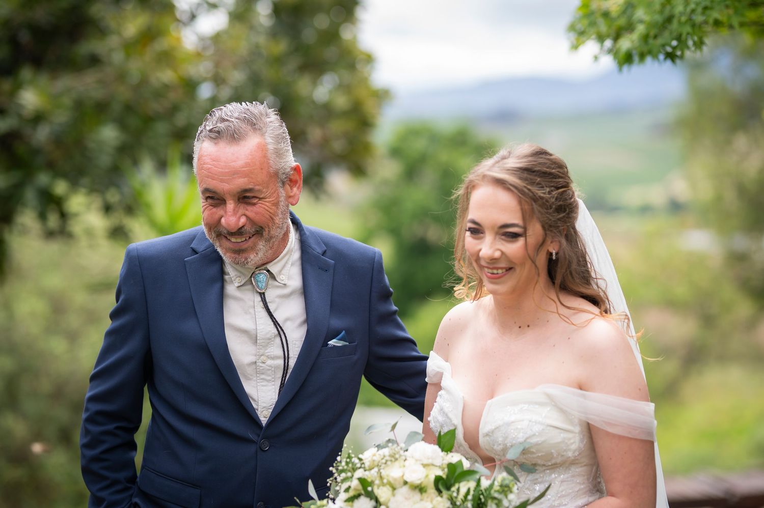 A bride and groom share joyful moments together outdoors during their wedding day photoshoot in a scenic natural setting.