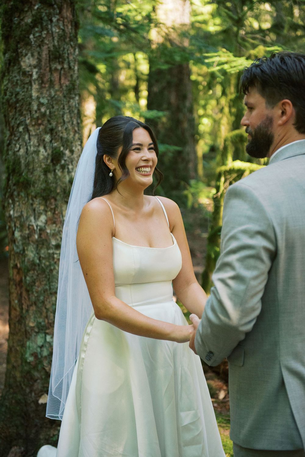 A couple shares a joyful first look moment in a sunlit forest setting during their wedding ceremony.