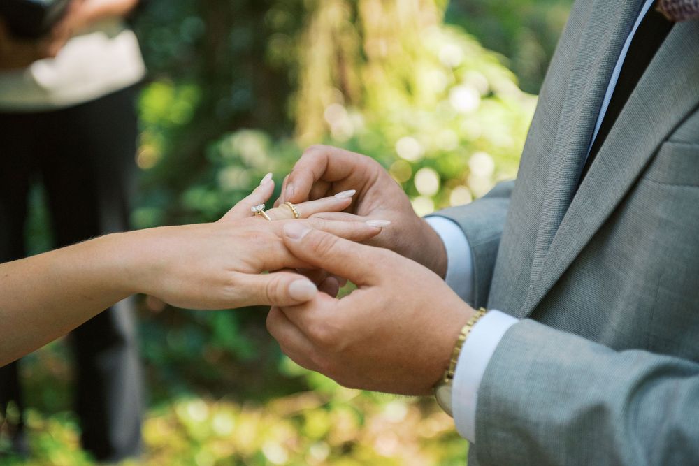 Close-up of hands during a wedding ring exchange ceremony outdoors.