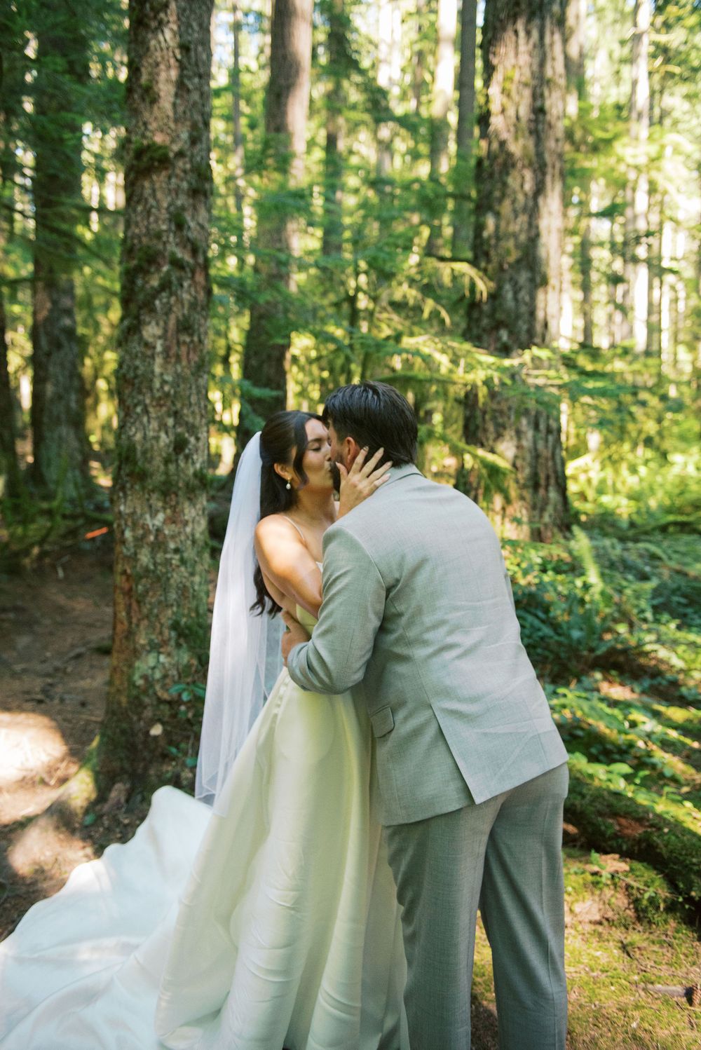 A romantic wedding kiss captured in a lush green forest setting.