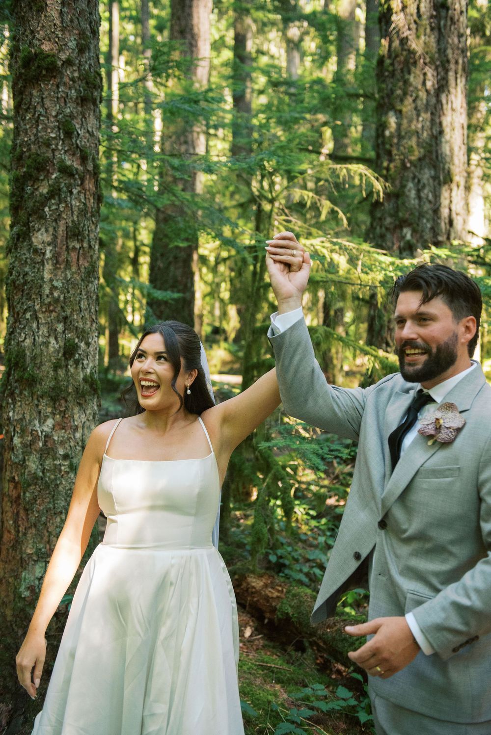A couple shares joyful moments together in a lush green forest setting during their wedding celebration.