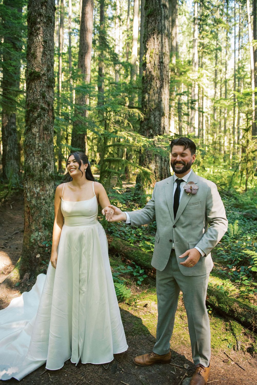 A couple poses together in a lush forest setting wearing elegant wedding attire.