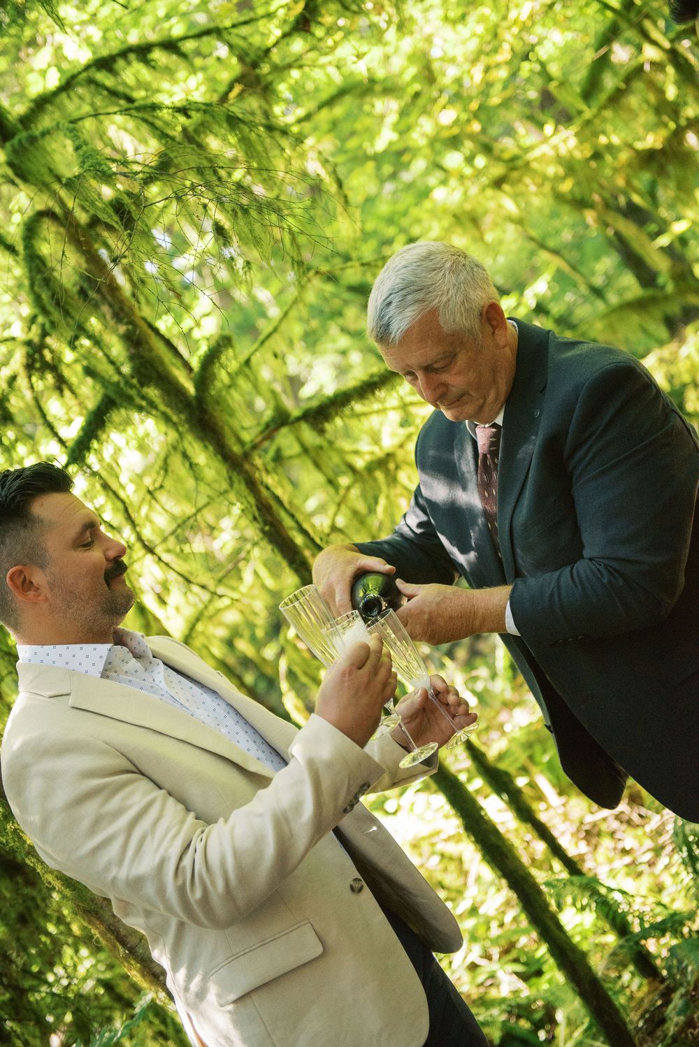 A sequence of photos showing a playful moment between two people in formal attire against a lush green outdoor backdrop.