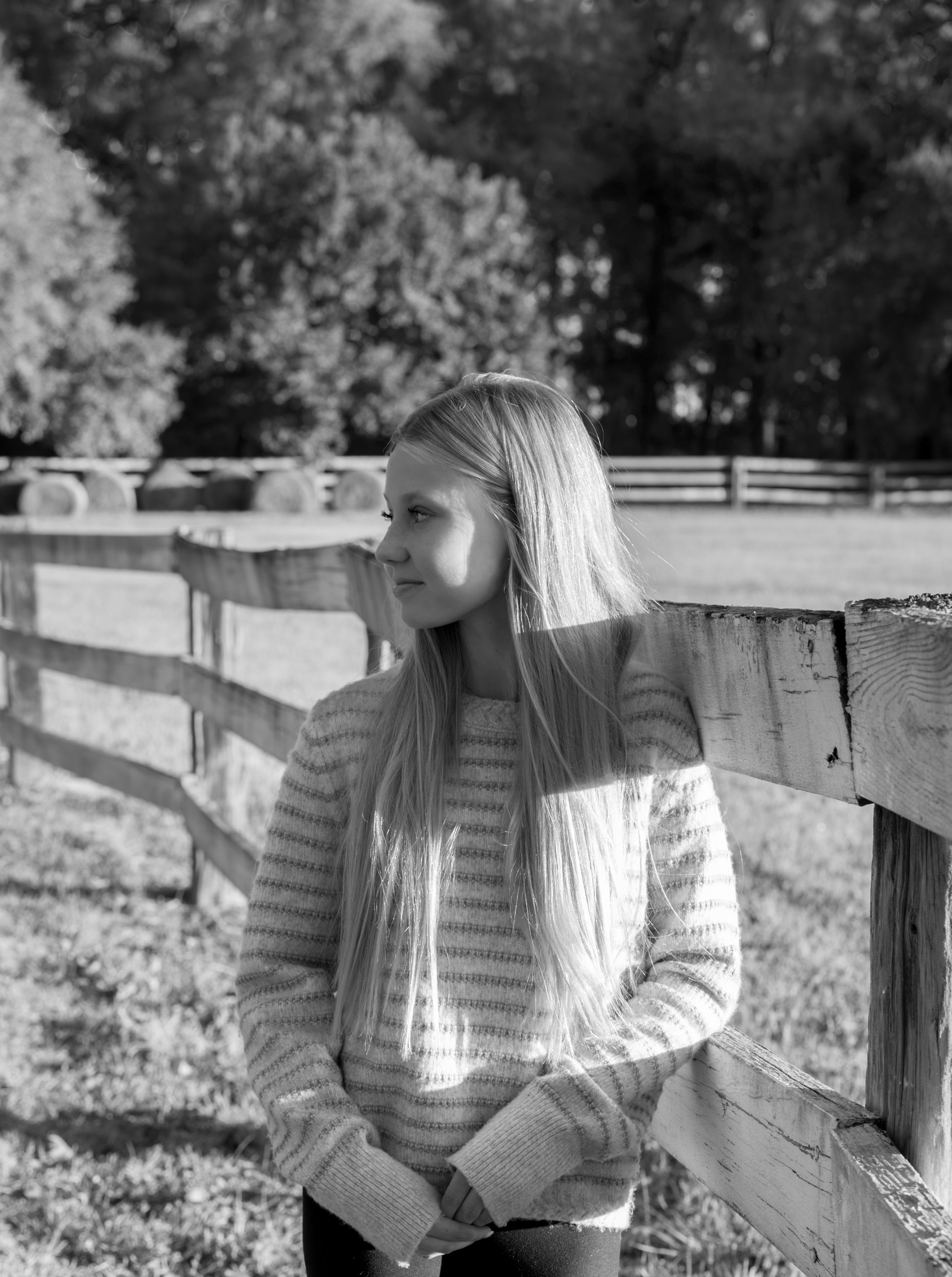 Black and white photo of person sitting on wooden fence in countryside.
