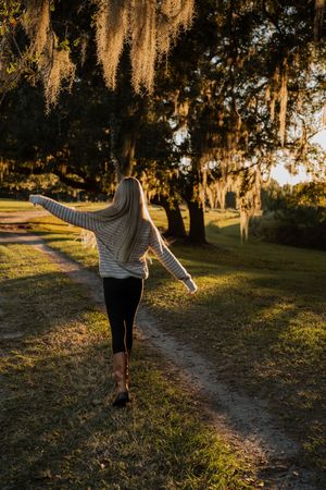 Figure walking along a tree-lined path at sunset wearing a striped top and dark pants.