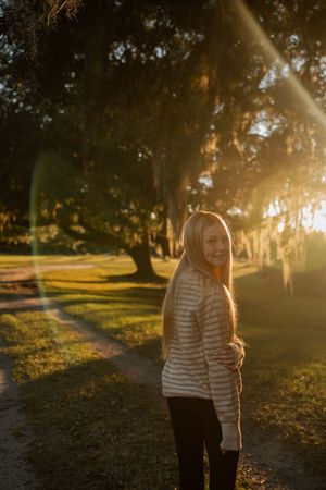 Silhouetted person standing in a park at sunset with sunlight streaming through trees.