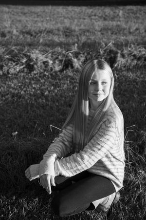 Black and white portrait of someone in a knit sweater sitting in grass.