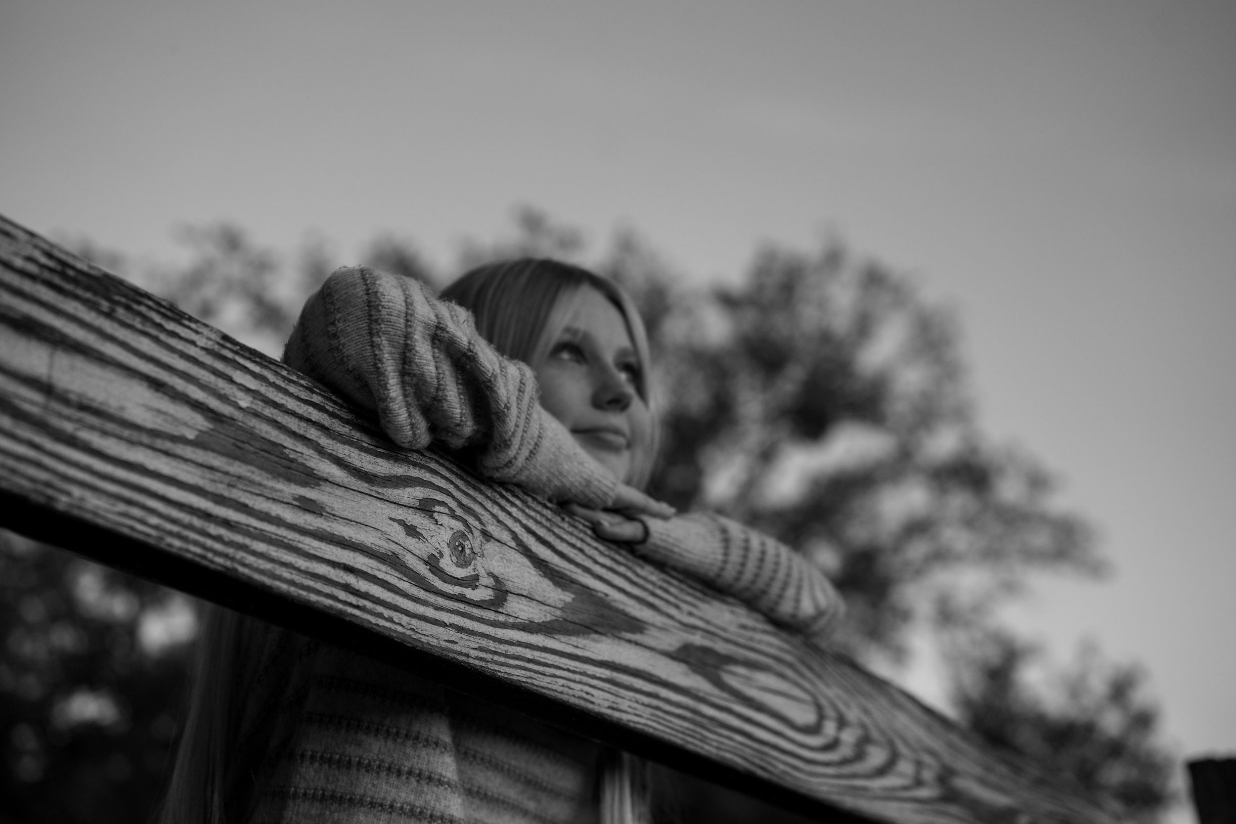 Black and white image of someone leaning on wooden railing outdoors.
