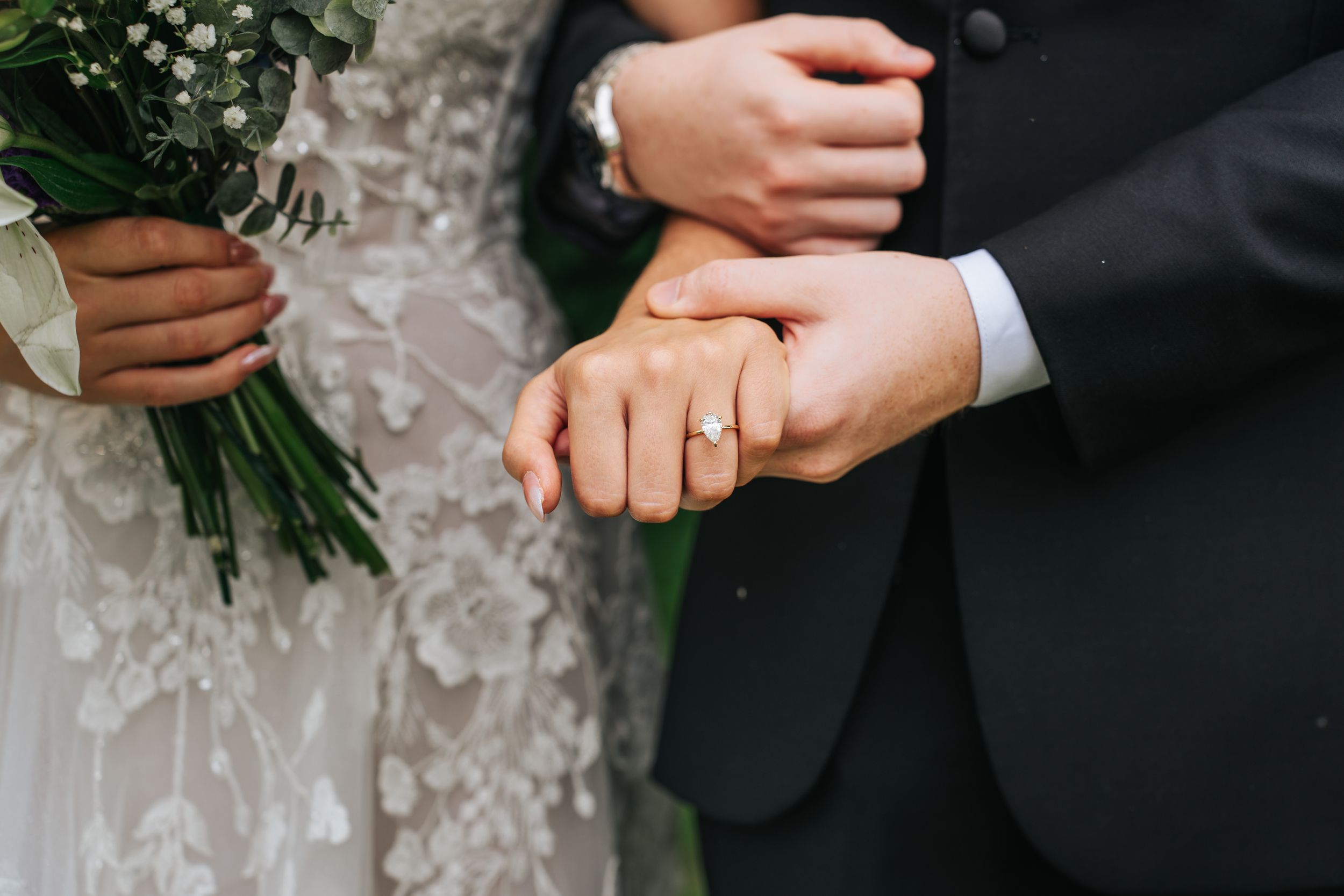 Close-up shot of hands holding a wedding bouquet with white and green flowers against a black suit jacket.