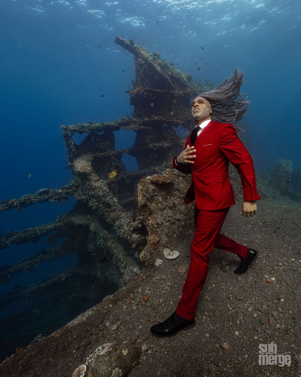 Underwater photography series showing a figure in red formal attire exploring a sunken shipwreck.