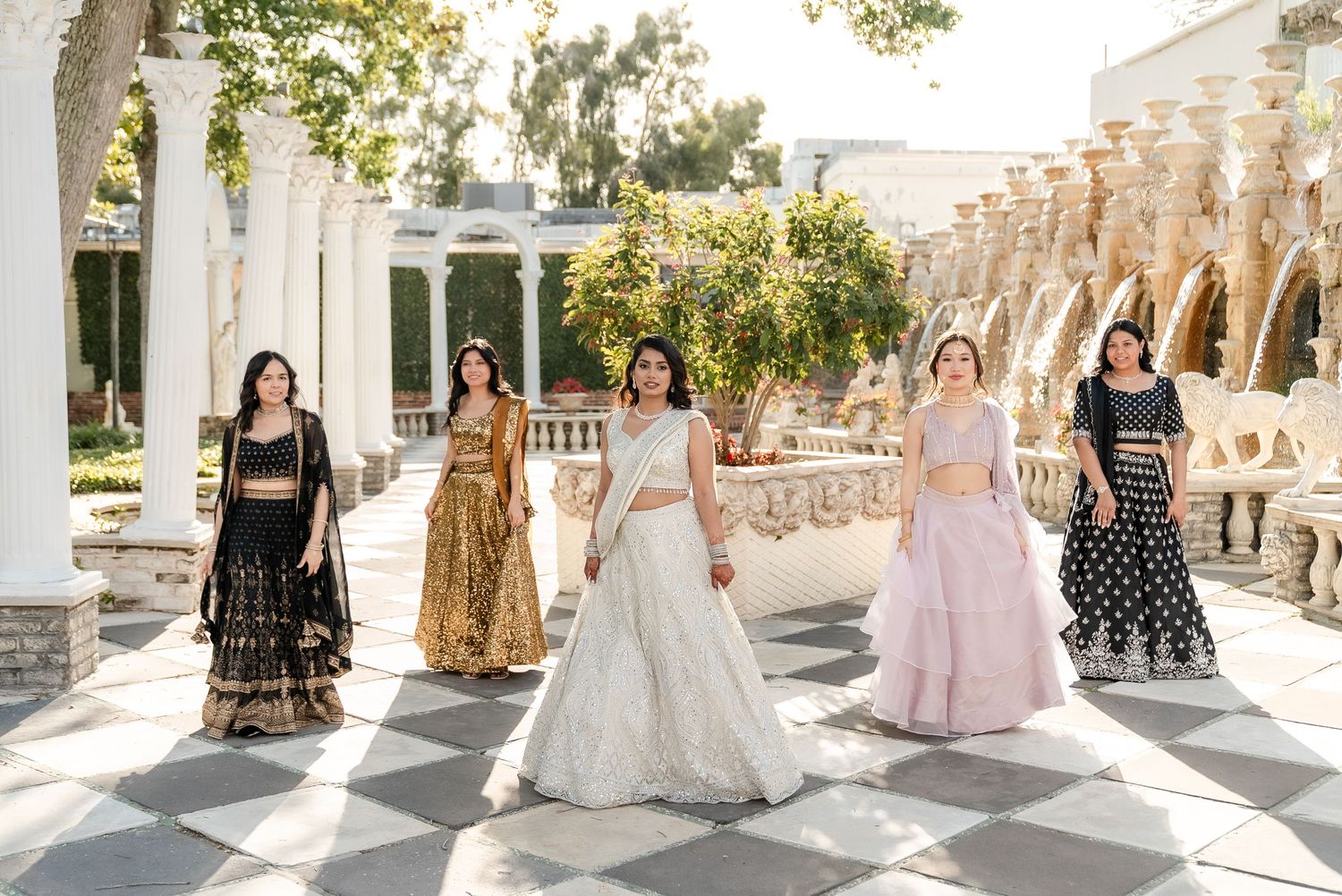 Elegant wedding dresses and formal gowns displayed in a row along a sunlit outdoor colonnade with white pillars.