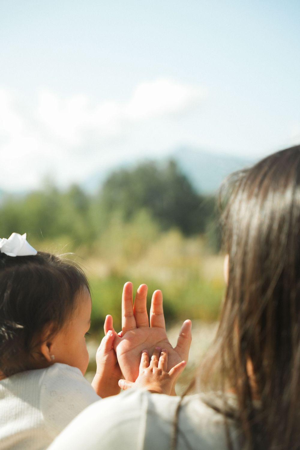 Children raise their hands against a bright sky in an outdoor setting during a sunny day.