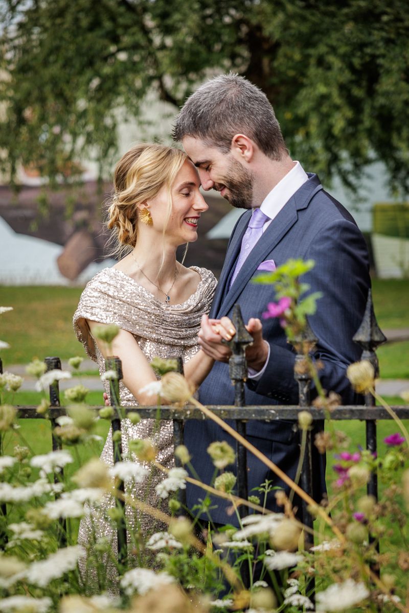 Romantic couple shares intimate moment in garden surrounded by blooming white flowers and greenery.