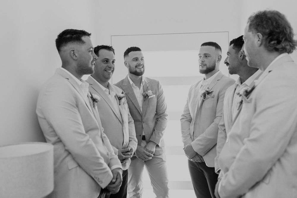 Groomsmen in light colored suits share candid moments while getting ready for a wedding ceremony.
