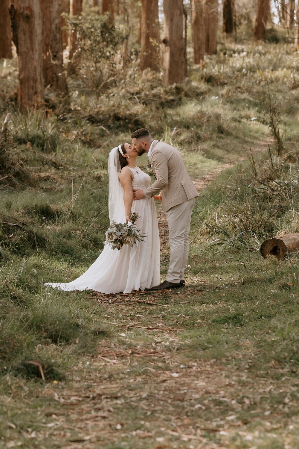 A romantic wedding couple shares intimate moments in a sun-dappled forest setting.