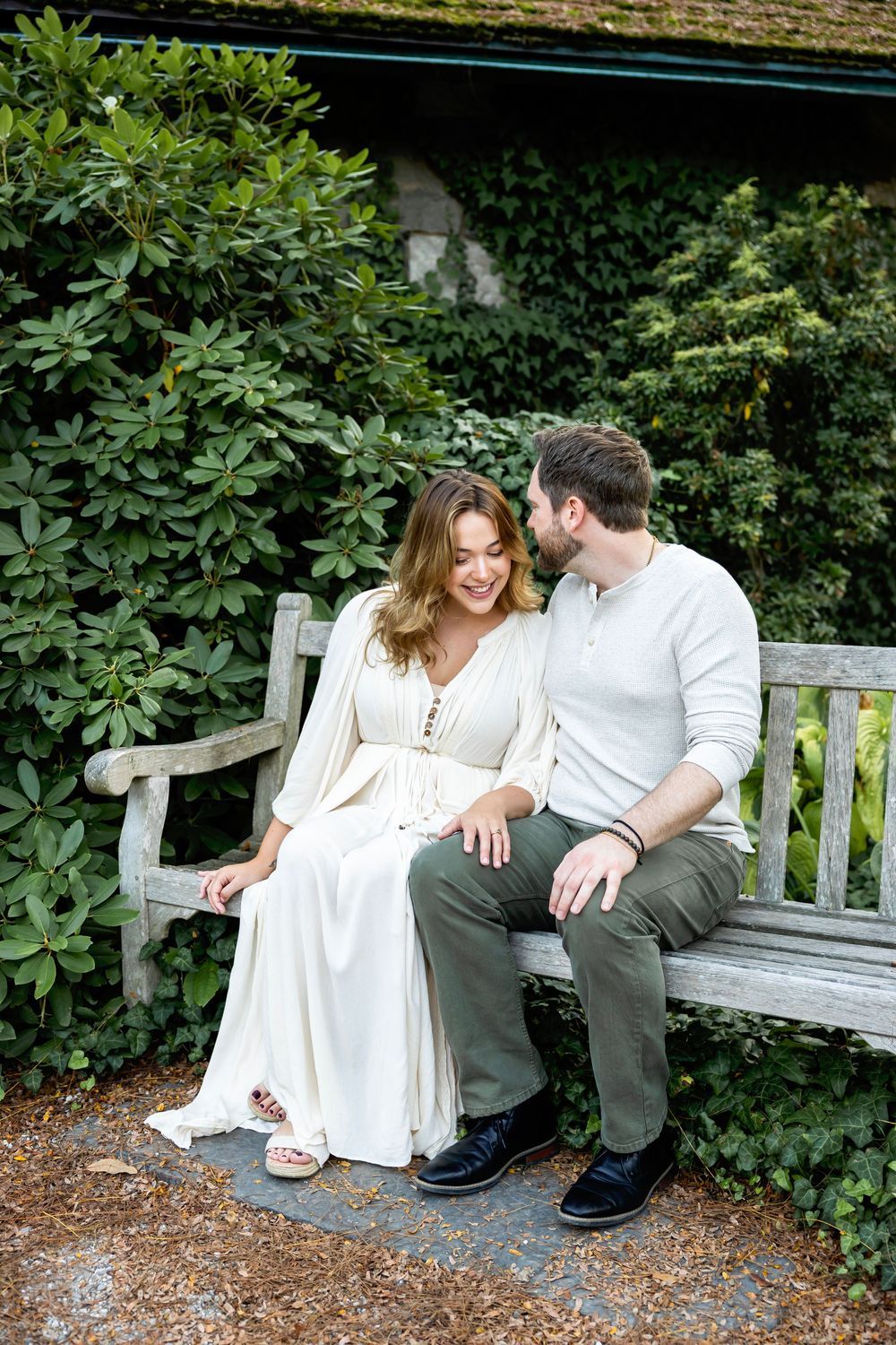 A couple shares a romantic moment together on a wooden garden bench surrounded by lush greenery.