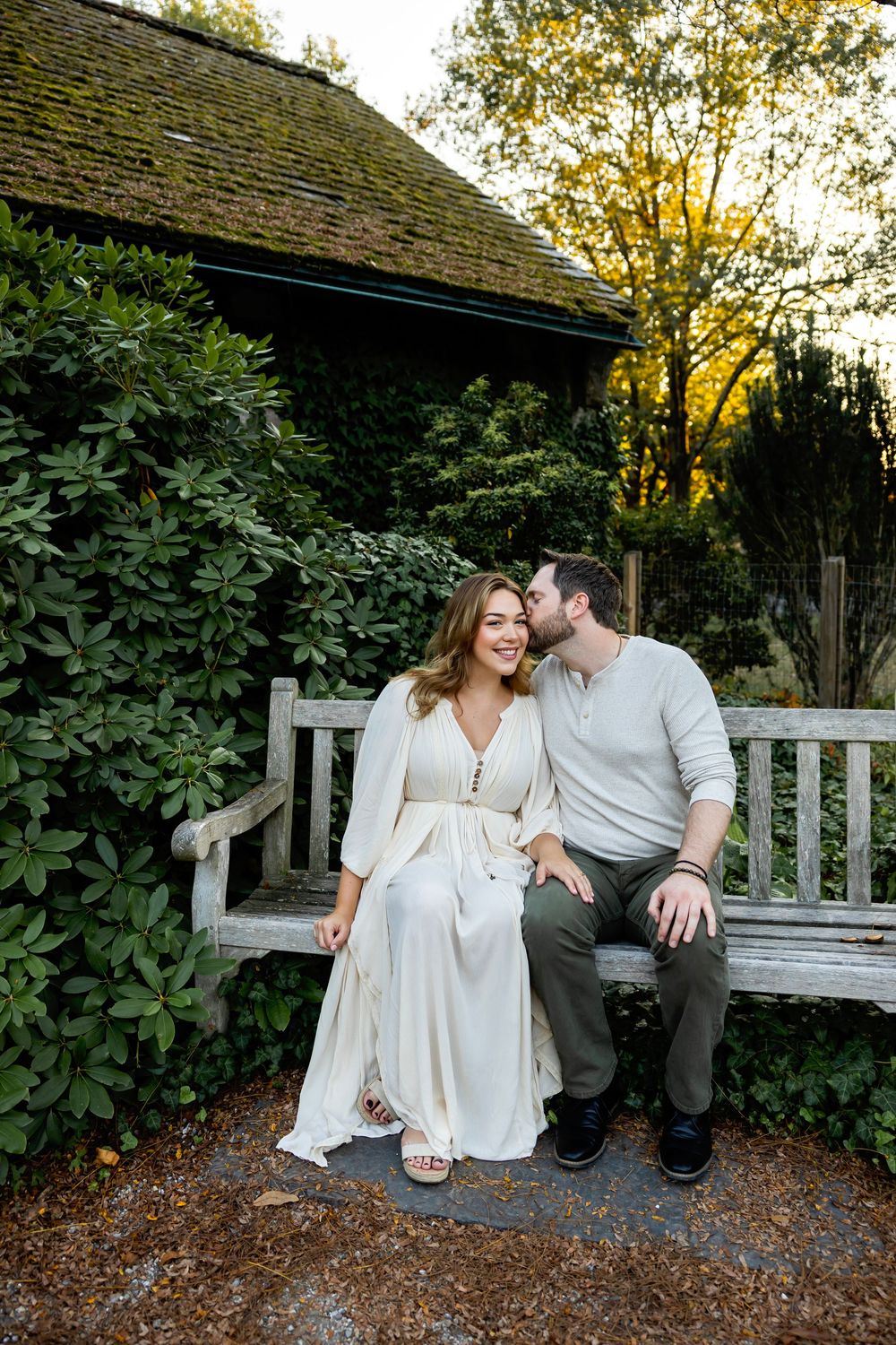 A romantic couple sits together on a wooden bench near a rustic garden shed at golden hour.