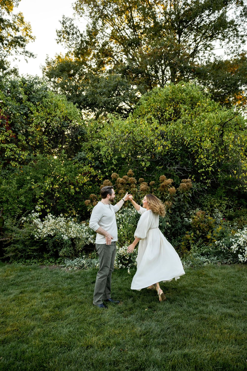 A couple dances playfully together on a green hillside surrounded by blooming trees and shrubs.