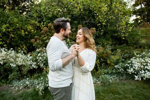 A couple shares a romantic dance together in a lush garden setting surrounded by blooming white flowers and greenery.