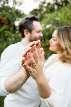 Close up of clasped hands with an engagement ring in a sunlit garden setting.